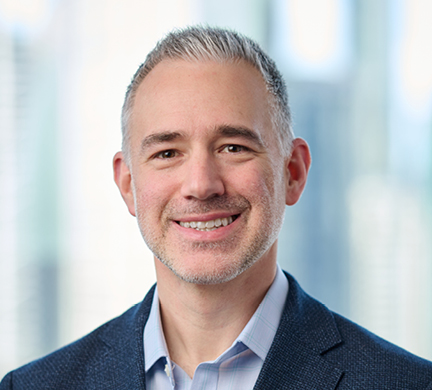 Professional headshot of Michael wearing a blue jacket and light blue shirt, against a softly blurred office background.