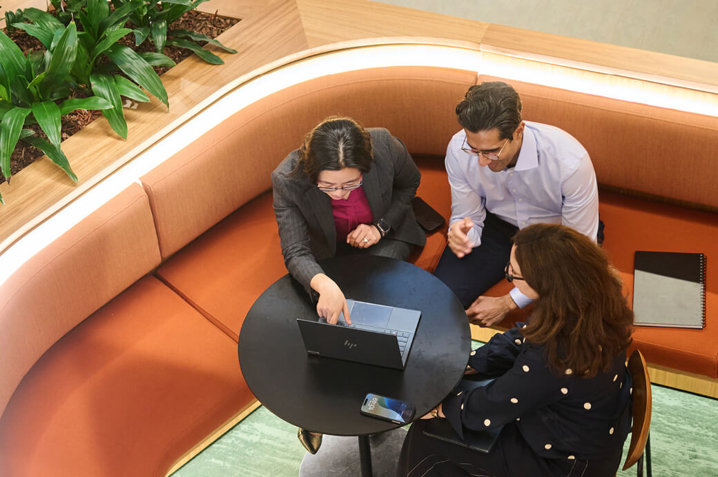 Top-down shot of three professionals collaborating around a laptop on a small round table.