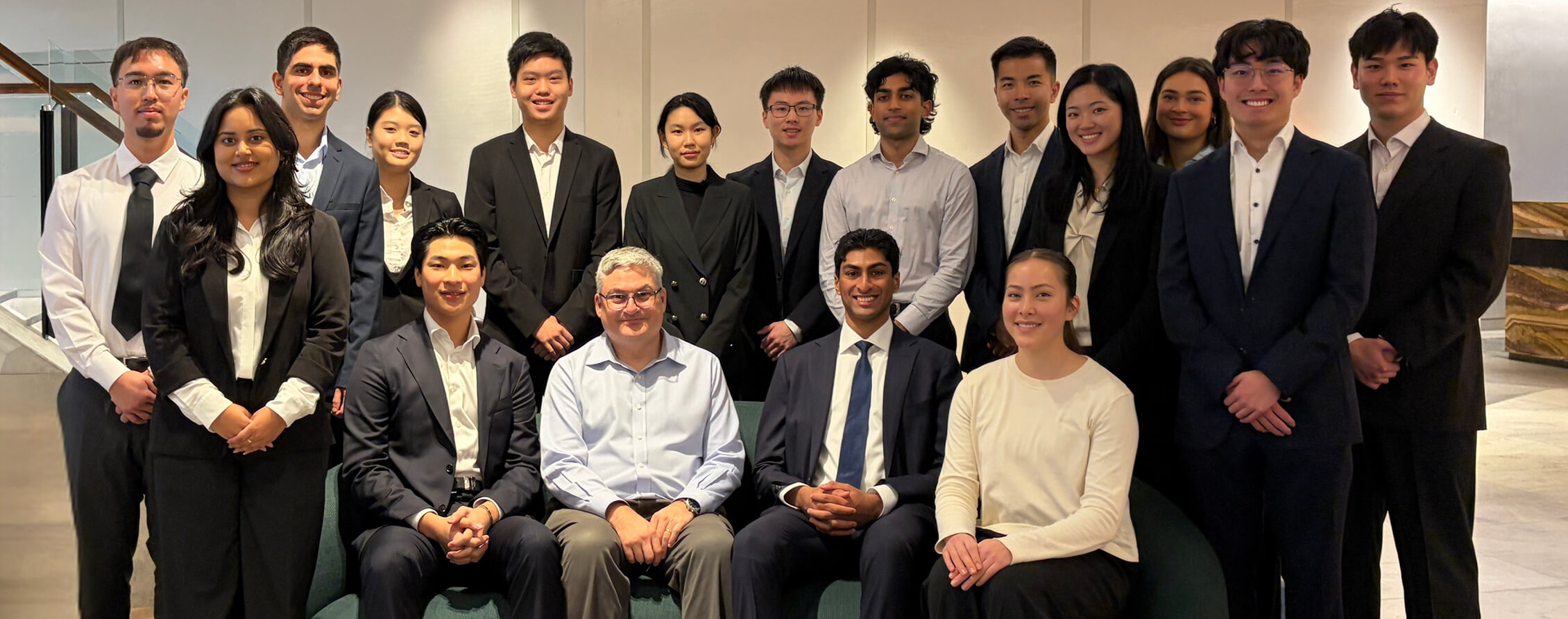 Group photo of Future Fund winter interns and CEO, Raphael Arndt, in business attire, gathered together in an office setting.