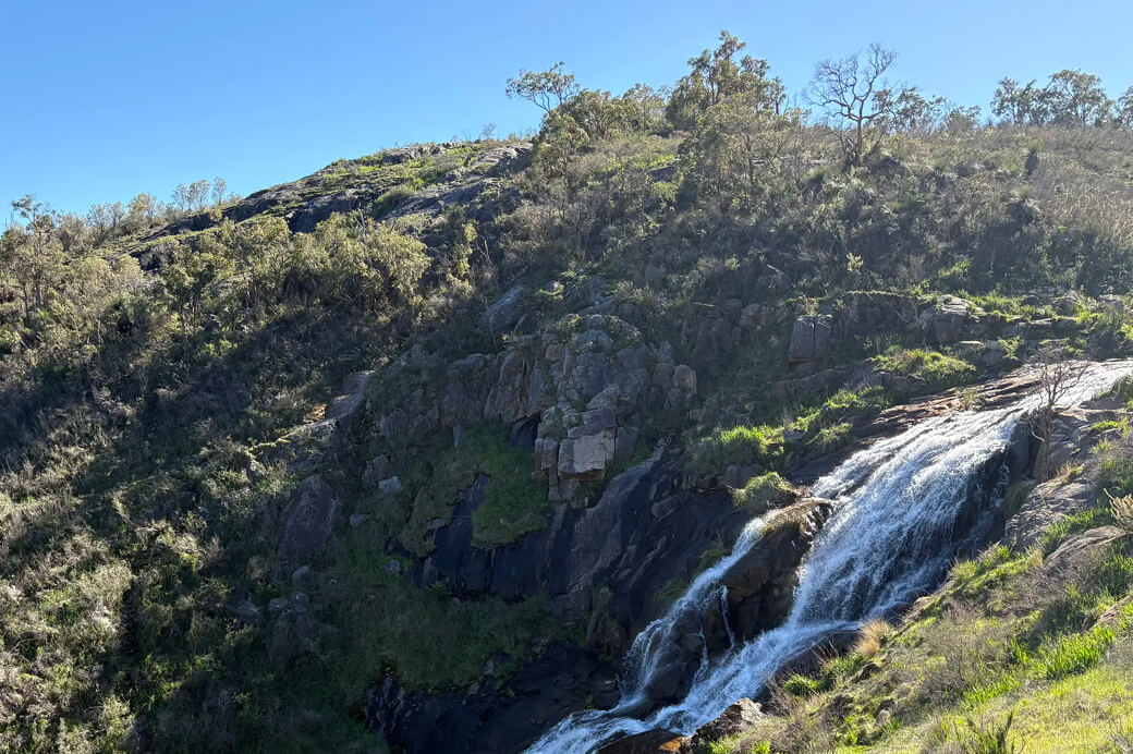 Landscape view of Lesmurdie Falls National Park in Western Australia, showing cascading water surrounded by native vegetation and rock formations.
